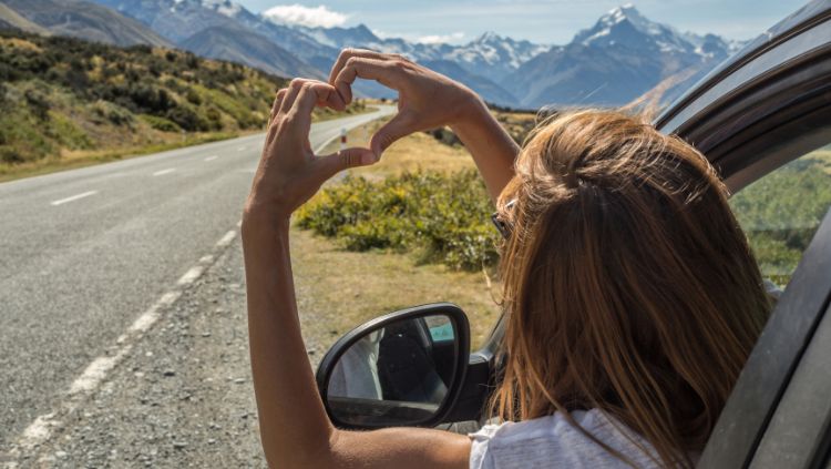 woman on a solo road trip, making the sign of a heart with her hands