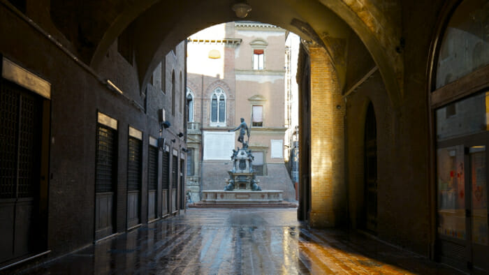 The Neptune Fountain is in the Piazza Maggore, the main square of the city. Stand in this portico (where you can see the fountain) at the cross road and turn away from the square and walk to the second cafe. This is where the more left-leaning locals go for a coffee or aperitivo.